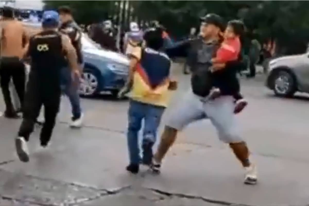 Foto: captura | En un clip se observa el momento en el que el hombre con un menor en brazos derriba a un aficionado del América.