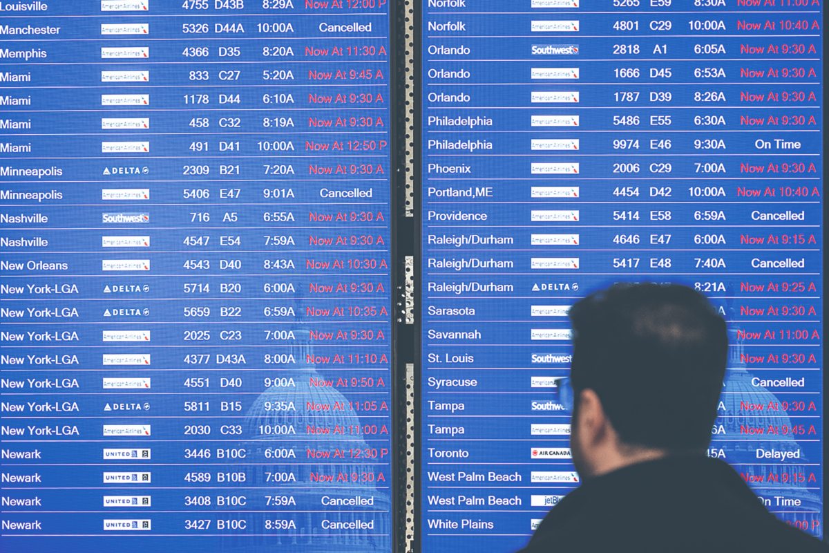 Pasajeros en el Aeropuerto Nacional Ronald Reagan de Washington en Arlington esperan y miran una pantalla de información de vuelos con la lista de cancelados y retrasados debido a una interrupción de la FAA