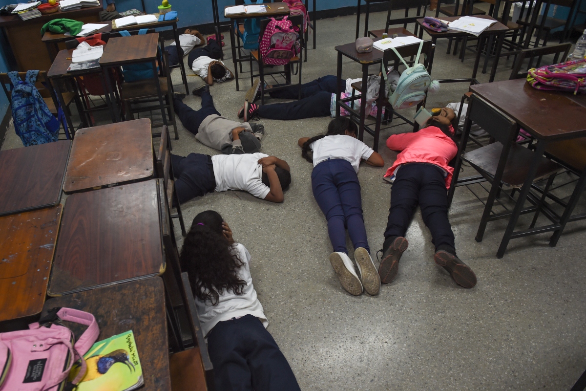 Alumnos cubren sus cabezas en el suelo durante un simulacro de tiroteo en la escuela Manuel Aguirre en el barrio de La Bombilla en Caracas